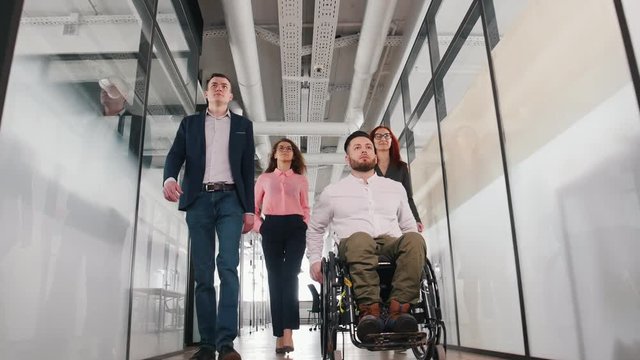 A successful business people walking through the bright corridor. A man in a wheelchair going first