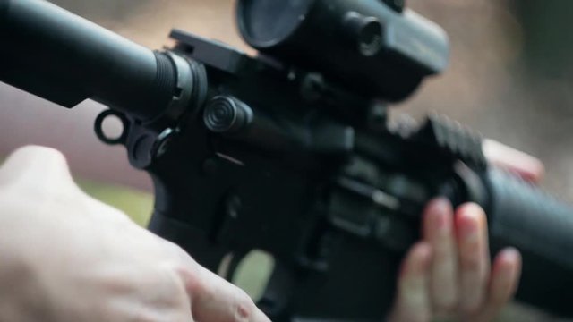 A man reloading an assault rifle, machine gun with red dot / reflex sight in the forest, and aimind the target in slow motion, Close up.