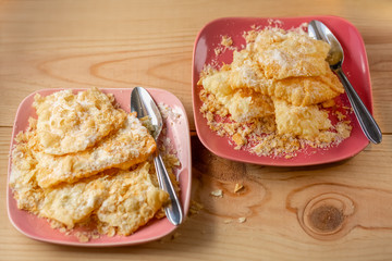 Crackled crispy cookies with powdered sugar. Tasty sweet cookies brushwood on a pink plate and teaspoons. Sweets on a plate and powdered sugar. Dessert. Top view.