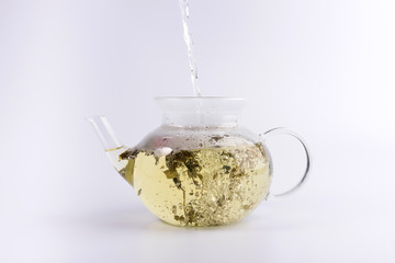 Pouring hot water to the glass teapot with herbal tea, isolated on white background