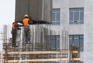 construction worker in a red vest puts armature on a residential building under construction
