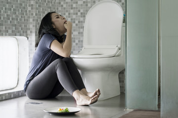 Woman forcing herself to vomit on bathroom - obrazy, fototapety, plakaty