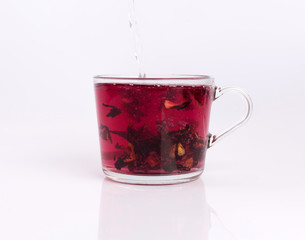 Pouring hot water to the glass cup with hibiscus tea, isolated on white background