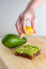 Woman hand squeezing half of lemon on whole bread avocado toast.