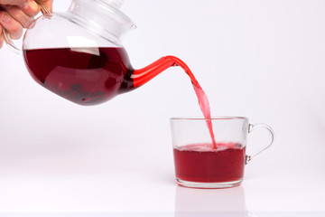 Glass teapot pouring hibiscus tea into cup isolated on white background