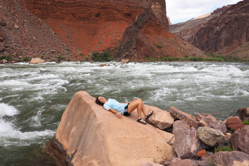 Young woman resting by the Colorado River at Hance Rapids during a multi-day hike in Grand Canyon National Park, Arizona.