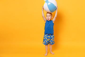 Kid boy 3-4 years old in blue beach summer clothes hold inflatable ball isolated on bright yellow...