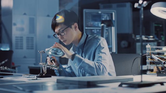 Professional Japanese Electronics Development Engineer in Blue Shirt is Soldering a Circuit Board in a High Tech Research Laboratory with Modern Computer Equipment.