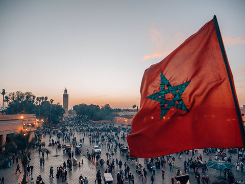 The waving flag of Morocco and the famous minaret of Marrakech at sunset.