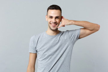 Portrait of smiling young man in casual clothes doing phone gesture like says call me back isolated on grey wall background in studio. People sincere emotions lifestyle concept. Mock up copy space.