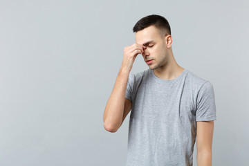 Portrait of exhausted young man in casual clothes keeping eyes closed, putting hand on nose isolated on grey wall background in studio. People sincere emotions, lifestyle concept. Mock up copy space.