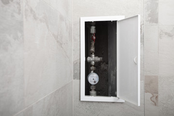 White plastic door or flap in the wall for water pipe service or repair. Renovation bathroom at home. Water meter.