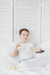 Fototapeta premium Boy eating popcorn sitting in bed and watching TV