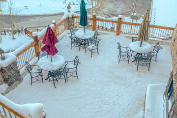 Tables with umbrellas and chairs on snowy balcony