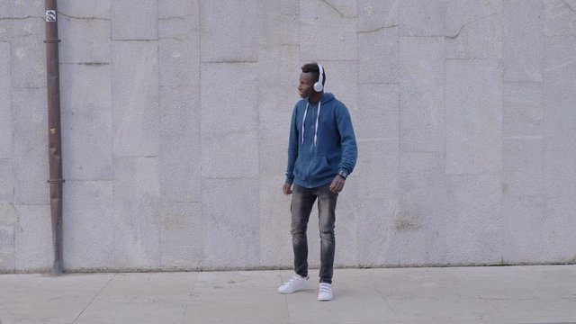 Modern black african guy using smartwatch and smartphone listening music-outdoor