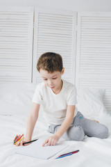 Naklejka premium Boy draws with colorful pencils sitting on the bed