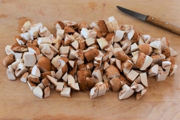 Sliced mushrooms next to a kitchen knife on a wooden board