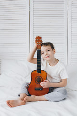Boy playing a small guitar sitting on the bed