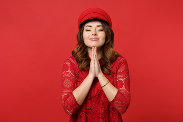 Portrait of pleading young woman in lace dress and cap holding hands folded praying isolated on bright red wall background in studio. People sincere emotions, lifestyle concept. Mock up copy space.