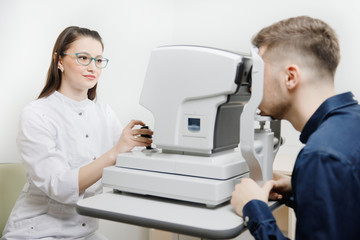 Female doctor ophthalmologist clinic checks eye vision of man on machine lamp.