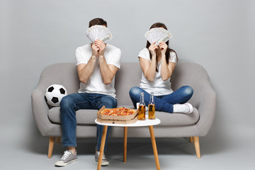 Couple woman man football fans cheer up support favorite team, covering face with fan of money in...