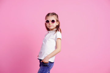 Portrait of beautiful smiling cute model in trendy round sunglasses. Casual 7 y.o. girl posing isolated on pink background.