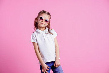 Portrait of beautiful smiling cute model in trendy round sunglasses. Casual 7 y.o. girl posing isolated on pink background.
