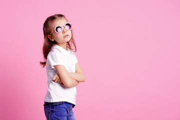 Portrait of beautiful smiling cute model in trendy round sunglasses. Casual 7 y.o. girl posing isolated on pink background.