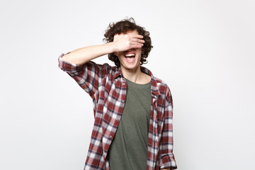 Portrait of cheerful laughing young man in casual clothes hiding, covering eyes with hand isolated on white wall background in studio. People sincere emotions, lifestyle concept. Mock up copy space.