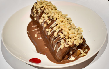 roll of crepe in a white ceramic plate with melted patterned light brown milk chocolate and white chocolate 