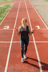 Fototapeta premium Sporty Lifestyle. Young woman on stadium standing on track with jump rope smiling cheerful top view