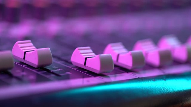 Hand of sound engineer working with fader on mixer console at music concert. Close up view. Colorful neon light