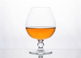 half filled glass with brown cognac on white surface