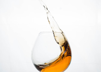 splash of brown cognac in transparent glass isolated on white 