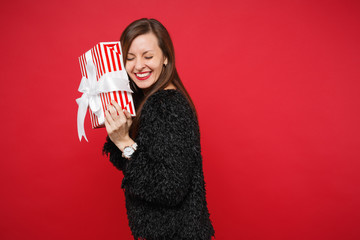 Happy young woman with closed eyes hold red striped present box with gift ribbon isolated on red...