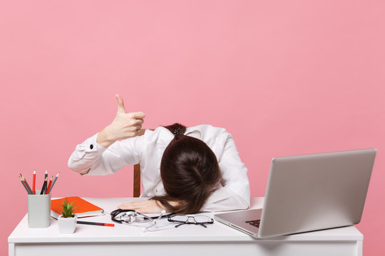 Female doctor laid her head down on desk, work on computer, medical document in hospital isolated on pastel pink wall background. Woman in medical gown stethoscope show ok. Healthcare medicine concept