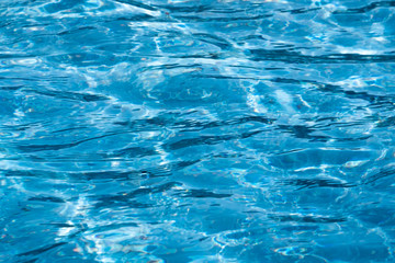 Blue and bright ripple water surface in swimming pool with sun reflection.