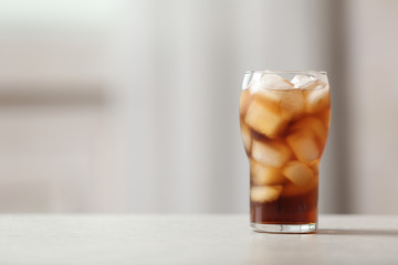Glass of cola with ice on table against blurred background, space for text