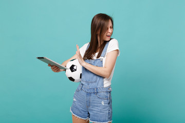 Disappointed girl football fan holding soccer ball, showing stop gesture with palm to tablet pc...
