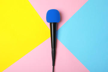 Modern microphone on color background, top view
