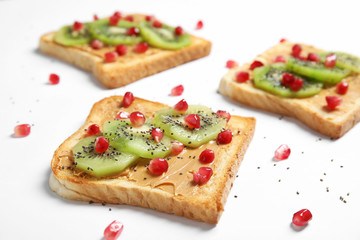 Tasty toasts with kiwi, peanut butter, pomegranate and chia seeds on white background