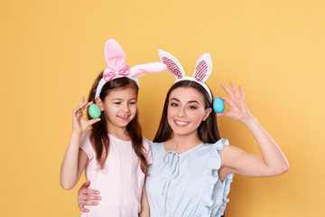 Mother and daughter in bunny ears headbands with Easter eggs on color background