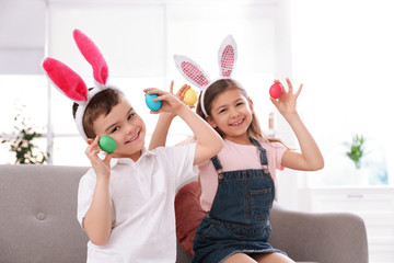 Cute little children in bunny ears headbands playing with Easter eggs at home