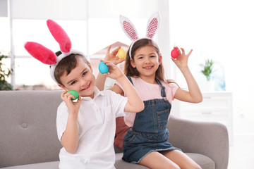 Cute little children in bunny ears headbands playing with Easter eggs at home