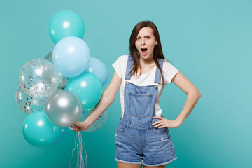 Shocked irritated young woman in denim clothes with opened mouth swearing celebrating hold colorful...