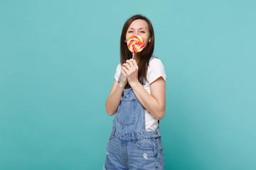Portrait of pretty young woman in denim clothes holding, covering mouth with colorful round...