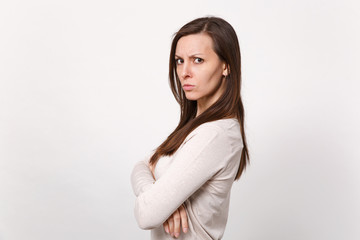 Fototapeta premium Side view of angry dissatisfied young woman in light clothes looking camera, holding hands folded isolated on white wall background. People sincere emotions, lifestyle concept. Mock up copy space.