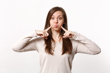 Fototapeta premium Portrait of funny young woman in light clothes pointing index fingers on blowing cheeks isolated on white wall background in studio. People sincere emotions, lifestyle concept. Mock up copy space.