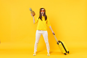 Excited traveler tourist woman in summer clothes hat hold fresh ripe pineapple fruit isolated on yellow orange background. Passenger traveling abroad on weekends getaway. Air flight journey concept.