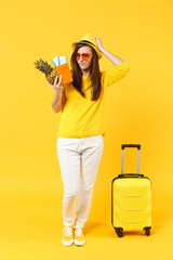 Preoccupied traveler tourist woman in hat hold passport tickets, fresh pineapple fruit isolated on yellow orange background. Passenger traveling abroad on weekends getaway. Air flight journey concept.